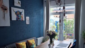 A dining area with a wooden table, blue upholstered bench, and a view of the garden through the window. - House Sleeps 6 With Wifi (Belfast)