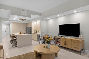 Une cuisine moderne dotée d’un îlot central, d’un coin repas avec une table ronde et d’un grand t éléviseur à écran plat fixé au mur.