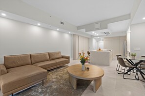 A modern living room with a sofa, a coffee table with flowers, a dining area with chairs, and a kitchen in the background. - Spacious Signature 3BR Villa for Golf & Family (Miami)