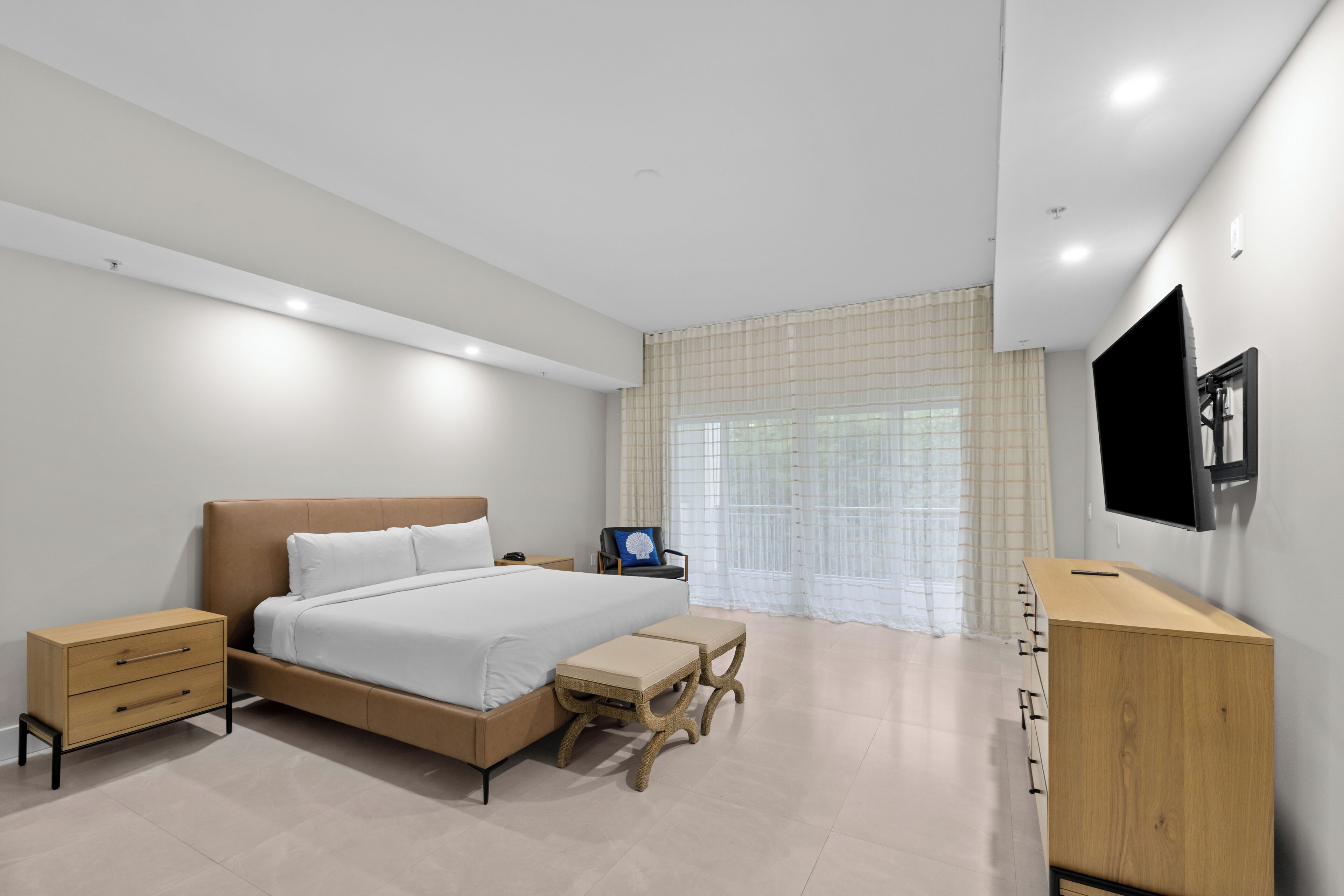 A bedroom with a bed, bedside tables, a desk, a chair, and a TV mounted on the wall.