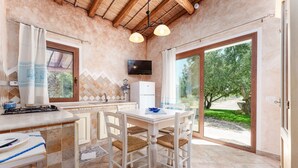 A kitchen with a dining area, a TV mounted above the counter, and a view of the outdoors through large sliding glass doors. - Apartment 'Angolo di Paradiso - Pavoncelle' with Sea View, Private Terrace & Air Conditioning (Orosei)