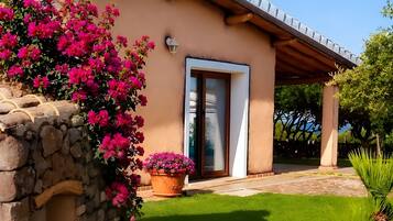 Une maison avec un mur en pierre, une pergola en bois et une pelouse bien entretenue.