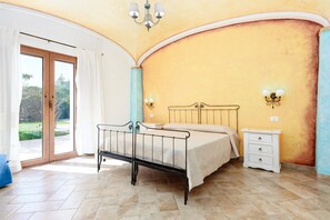 Ein Schlafzimmer mit Bett, Nachttisch, Lampe und einer Schiebeglastür, die auf einen Balkon führt.