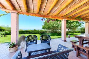 Eine Terrasse im Freien mit einer Holz-Pergola, Sitzgelegenheiten und Blick auf einen gepflegten Garten.