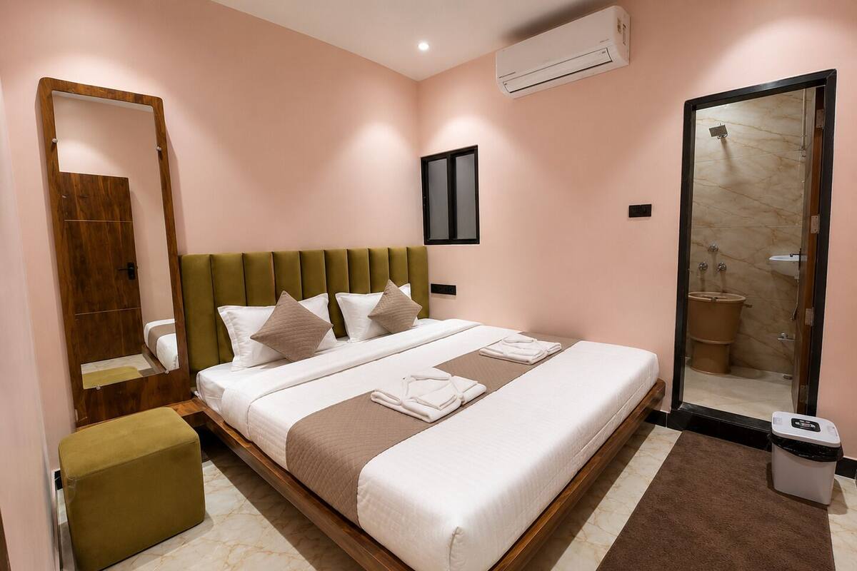 A hotel room with a bed, a mirror, a wardrobe, an air conditioning unit, and a bathroom visible through a glass door.