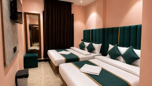 Habitación de hotel con tres camas, un televisor, un espejo y un bote de basura.