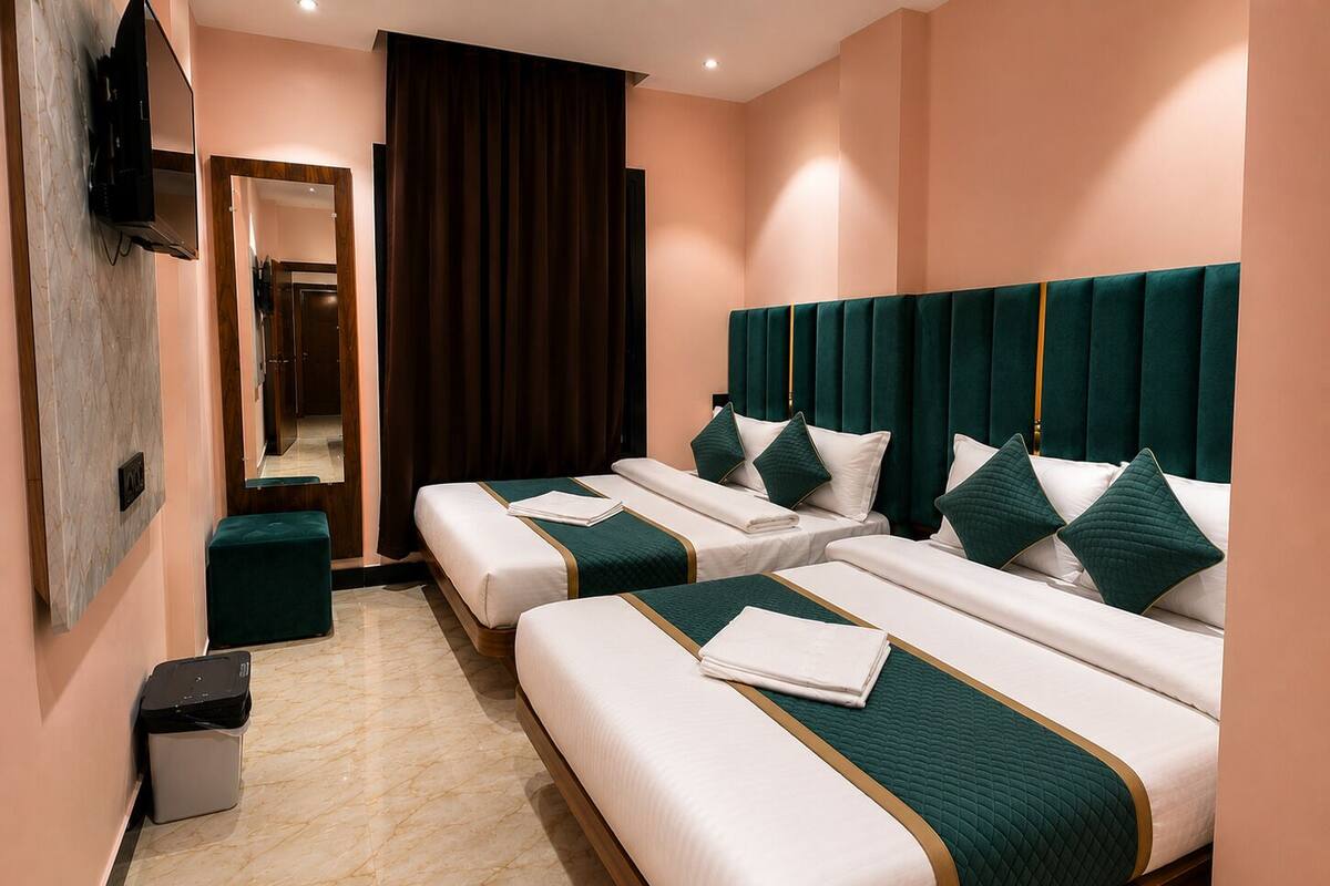 A hotel room with three beds, a TV, a mirror, and a trash bin.