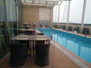 A poolside area with tables and chairs, a pool, and a decorative wall. - Ramaya The Boutique Hotel Haryana (Rohtak)