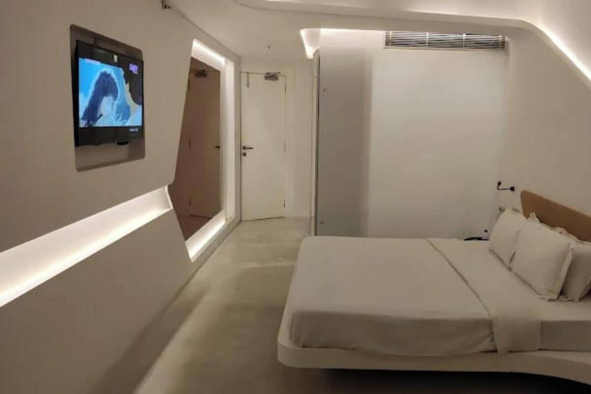 Ein Schlafzimmer mit einem Bett, einem an der Wand montierten Fernseher und einer Tür zu einem weiteren Raum.