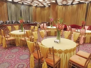 Ein Festsaal mit runden Tischen, Stühlen und floralen Tischdekorationen.