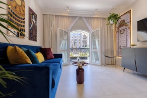 Un salon moderne avec un canapé bleu, une table basse en verre et une vue sur un immeuble d’habitation, visible à travers de grandes fenêtres.