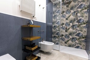 Une salle de bain avec une baignoire blanche, une cabine de douche en verre et un mur orné d’un motif de feuilles tropicales.