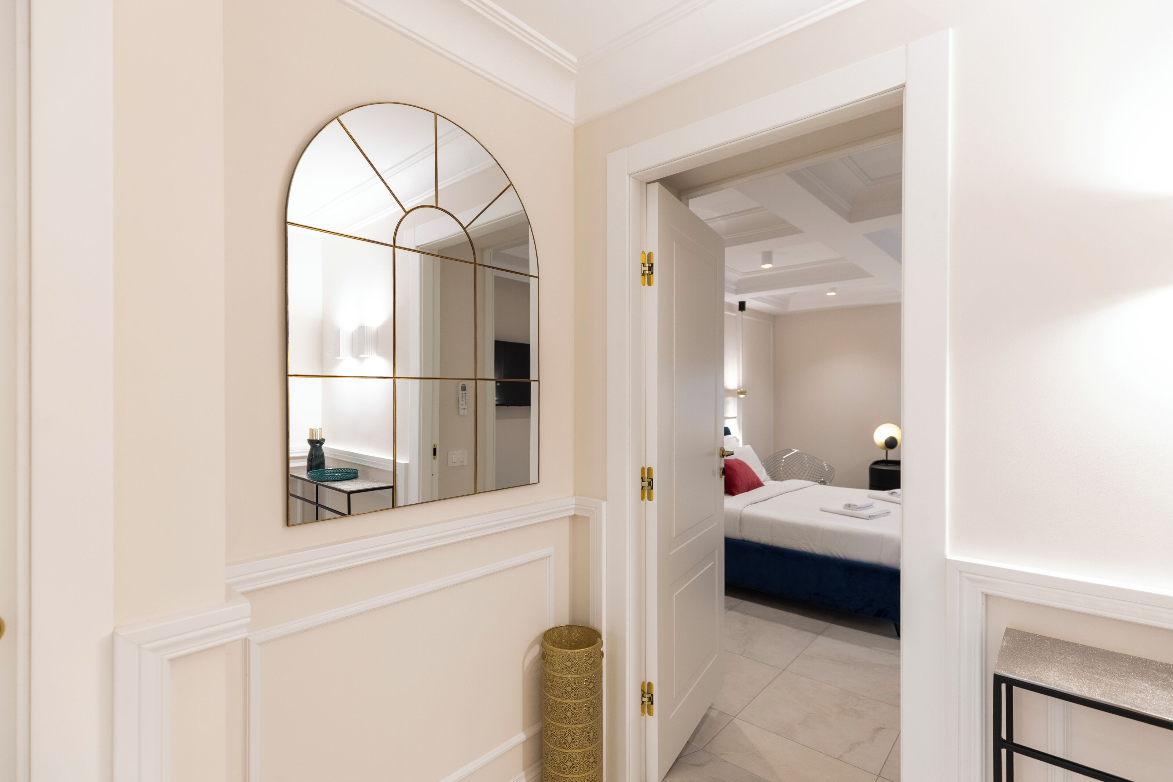 Een gang die leidt naar een slaapkamer met een bed, nachtkastje en een lamp.