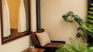 A corner room with a window, a chair, a small table, and a potted plant.