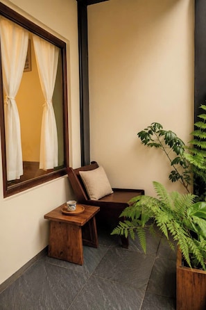 Habitación de esquina con ventana, una silla, una mesita y una planta en maceta.