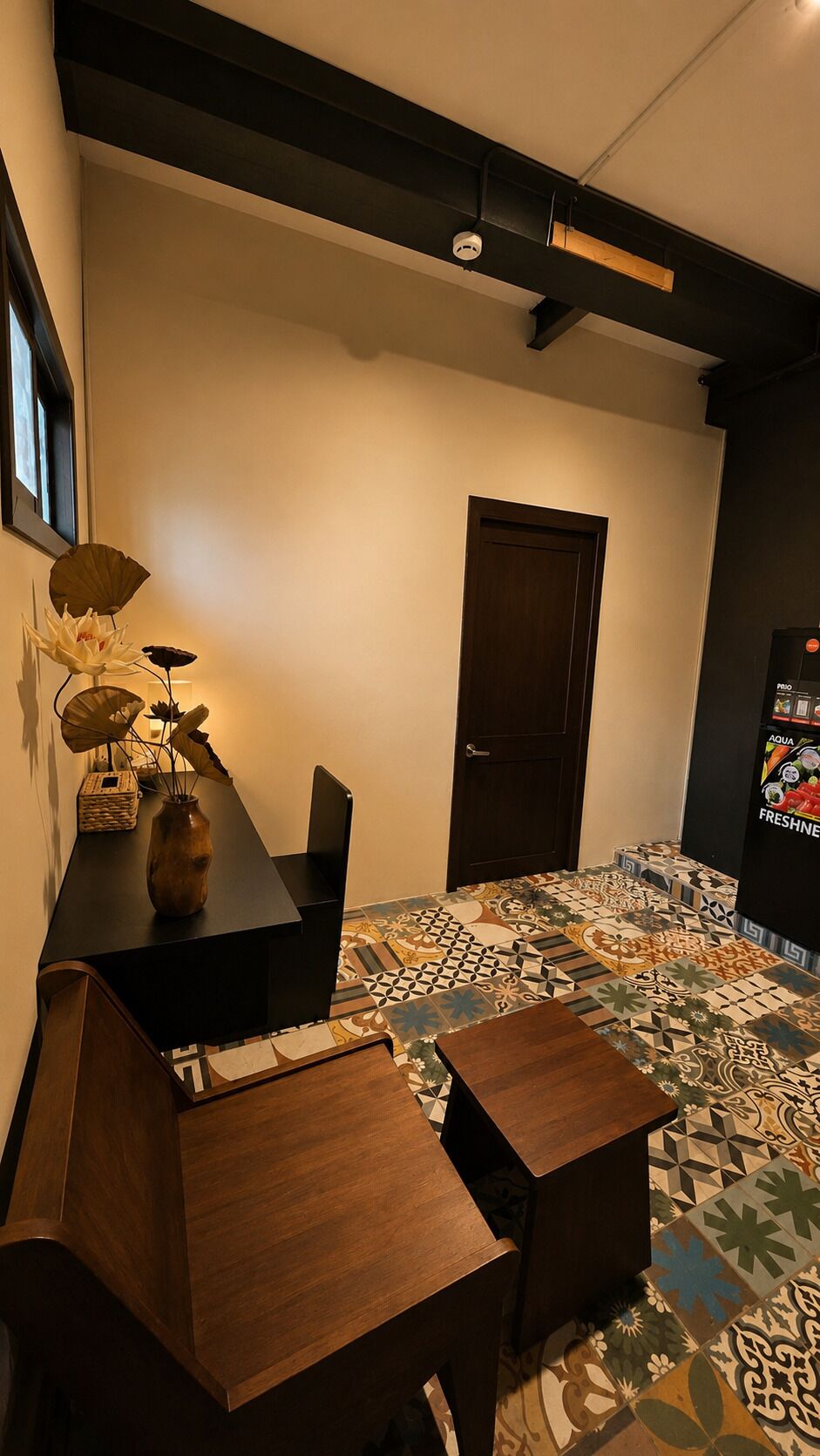 Una habitación con una mesa de madera oscura, un florero con flores, un suelo estampado y una puerta.