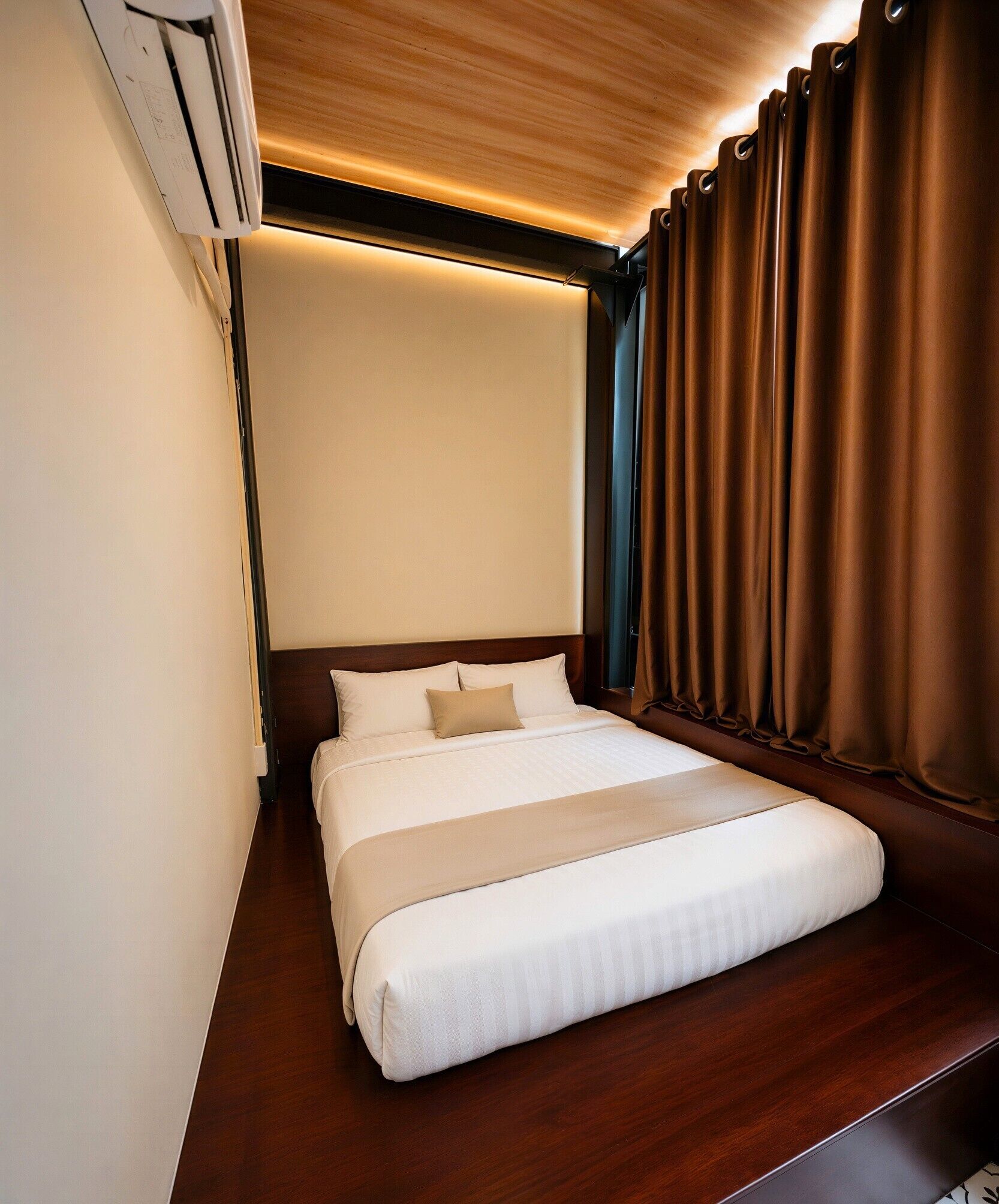Una habitación de hotel con cama, cabecero de madera, cortinas marrones y una lámpara del techo.