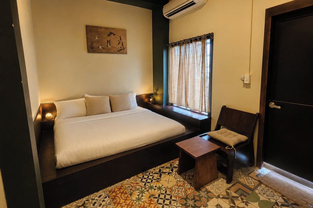 A bedroom with a bed, bedside table, chair, and a window with curtains.