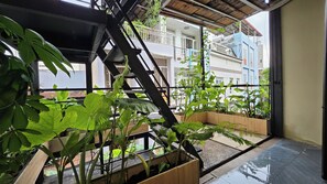 Un balcón con plantas en macetas, una escalera de metal y vistas de edificios cercanos.