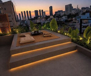 A rooftop terrace with a seating area, steps, and a cityscape view at dusk. - Nha Cuoi Boutique Serviced Aparthotel (Ho Chi Minh City)