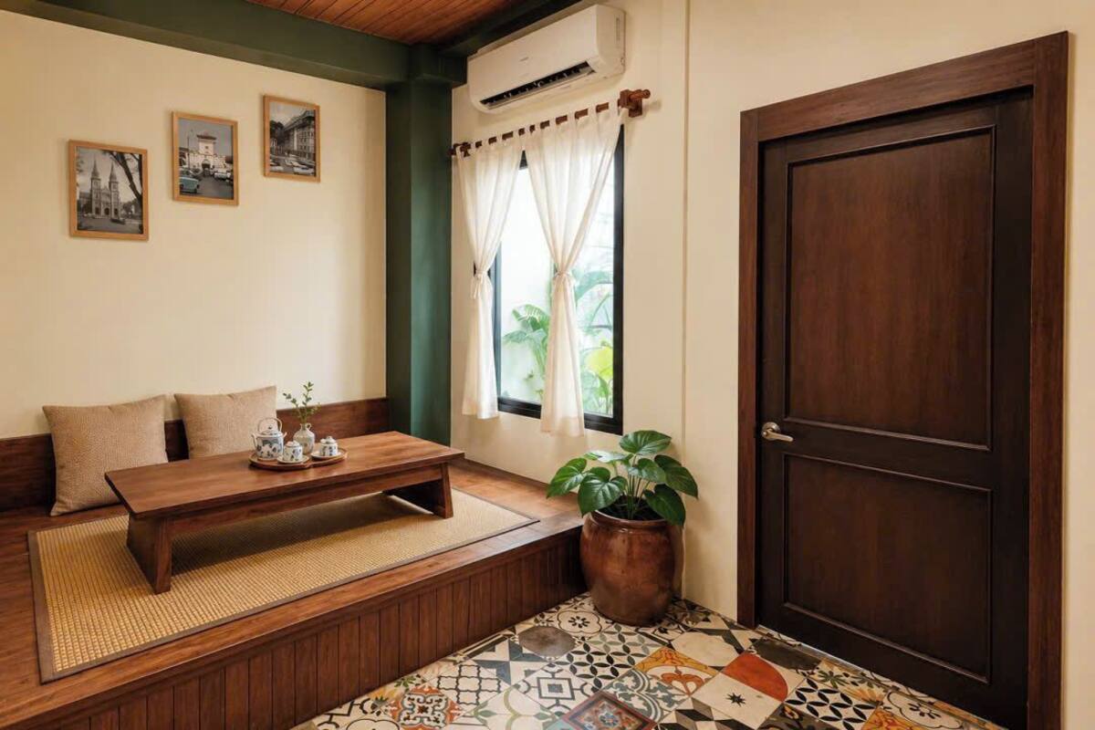 Ein Zimmer mit einer hölzernen Bank, einem kleinen Tisch mit Teekannen, einer Topfpflanze und einer Tür.