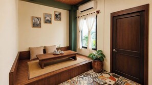 Quarto com um banco de madeira, uma mesa pequena com bules, uma planta em vaso e uma porta.