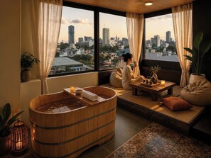 A room with a wooden bathtub, a sofa, a table with tea set, and a view of a cityscape. - Nha Cuoi Boutique Serviced Aparthotel (Ho Chi Minh City)