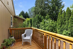 A wooden deck with a white wicker chair, surrounded by dense greenery and tall trees. - PNW Oasis w/PVT Ste. nr Nike/Intel-Pet Friendly (Aloha)
