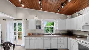 Cocina con armarios blancos, encimera negra y ventana con vistas a la vegetación.