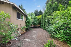 A residential backyard with a house, a garden hose, and dense greenery. - Family-Friendly Aloha Home Near Intel & Nike (Aloha)