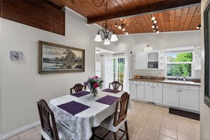 A dining area with a table, chairs, a chandelier, a painting, and a kitchen with cabinets and a window. - PNW Oasis w/PVT Ste. nr Nike/Intel-Pet Friendly (Aloha)