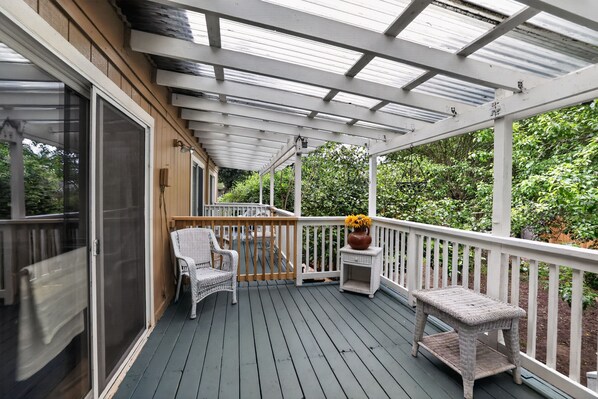 A covered outdoor deck with a railing, a chair, a small table, and a potted plant. - Family-Friendly Aloha Home Near Intel & Nike (Aloha)