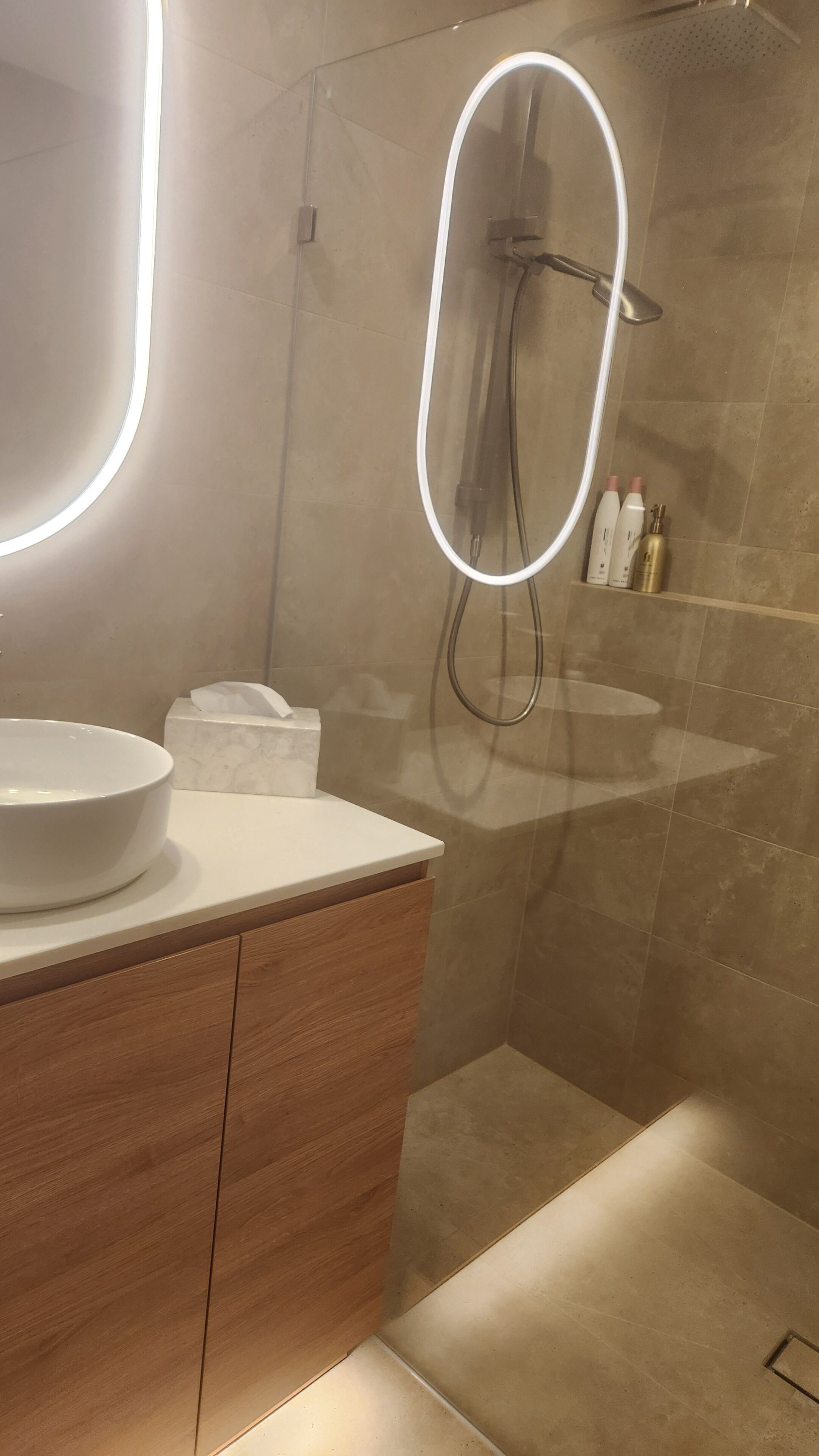 A modern bathroom with a large mirror, a round sink, and a shower area.