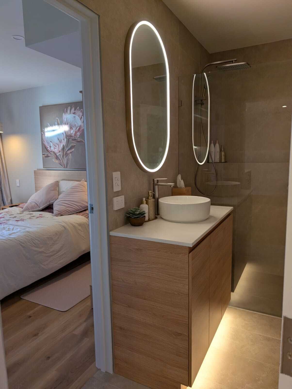 A modern bathroom with a large oval mirror, a round sink, and a shower area.