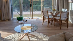 Un salon spacieux avec une table en verre, des chaises en bois, un canapé et une vue dégagée grâce à de grandes fenêtres.