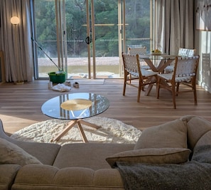 Amplia sala de estar con una mesa de vidrio, sillas de madera, un sofá y vistas panorámicas a través de amplias ventanas.