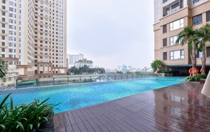 Ein Schwimmbecken mit Holzterrasse, umgeben von hohen Wohnhäusern.