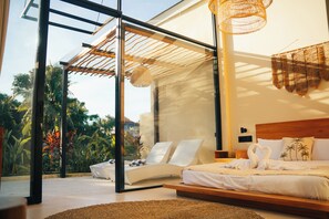 Une chambre moderne avec une porte en verre donnant sur un balcon, un lit avec du linge de lit blanc et un luminaire suspendu au plafond, fait de fibres tressées.