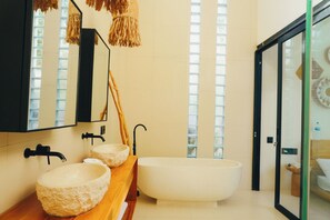 Une salle de bain moderne avec une baignoire sur pieds, deux vasques en pierre, un grand miroir et un luminaire suspendu.