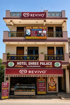 Un hotel de varios pisos con balcones, un cartel que anuncia un restaurante vegetariano estricto, y un número de contacto.