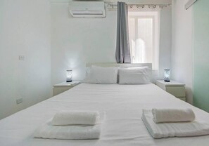 Ein Schlafzimmer mit einem Bett, zwei Nachttischen mit Lampen, einem Fenster mit Vorhängen und einer Klimaanlage.