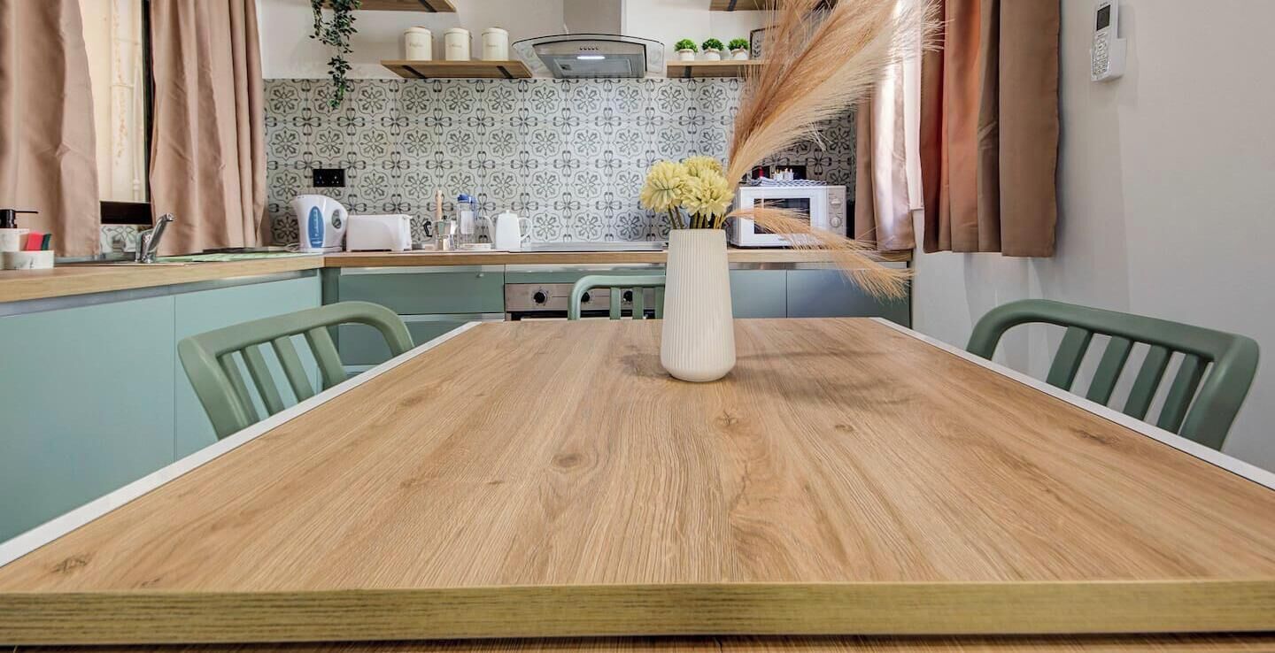 Une table à manger avec des chaises, un vase rempli de fleurs, une cuisine en arrière-plan et un téléphone fixé au mur.