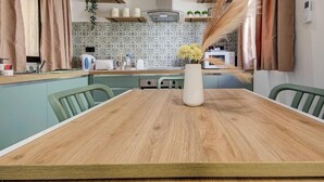 A dining table with chairs, a vase with flowers, a kitchen in the background, and a wall-mounted phone. - 2BR Maisonette Near St. Paul`s Bay & Beaches (St. Paul`s Bay)