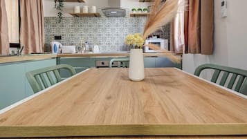 Une table à manger avec des chaises, un vase rempli de fleurs, une cuisine en arrière-plan et un téléphone fixé au mur.