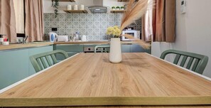 Ein Esstisch mit Stühlen, eine Vase mit Blumen, eine Küche im Hintergrund und ein an der Wand befestigtes Telefon.