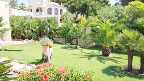 A garden with palm trees, a stone wall, and a building with arched windows. - Villa- Calypso in J vea (Javea)