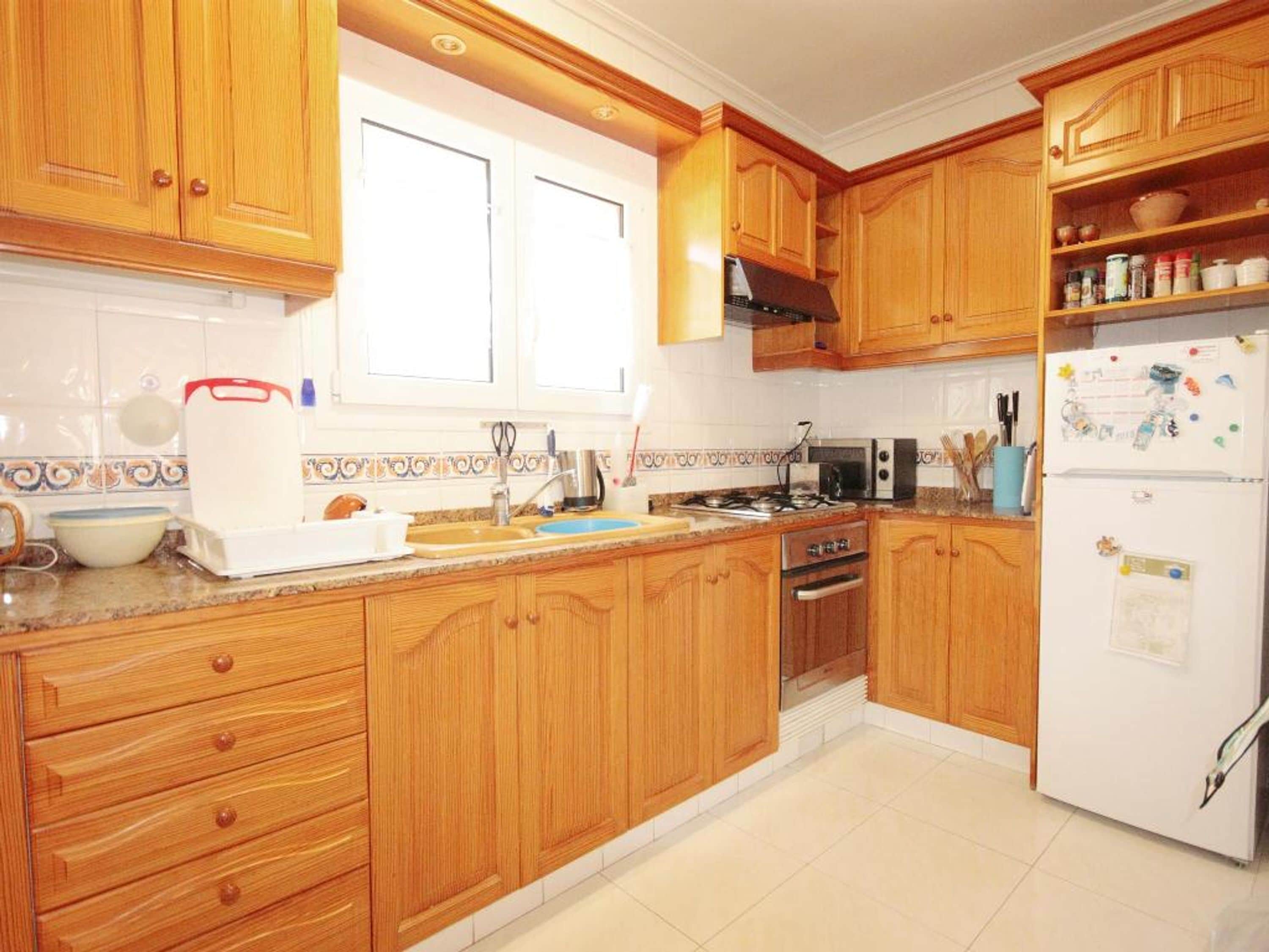 Une cuisine avec des meubles de rangement en bois, une cuisinière, un évier et un réfrigérateur.