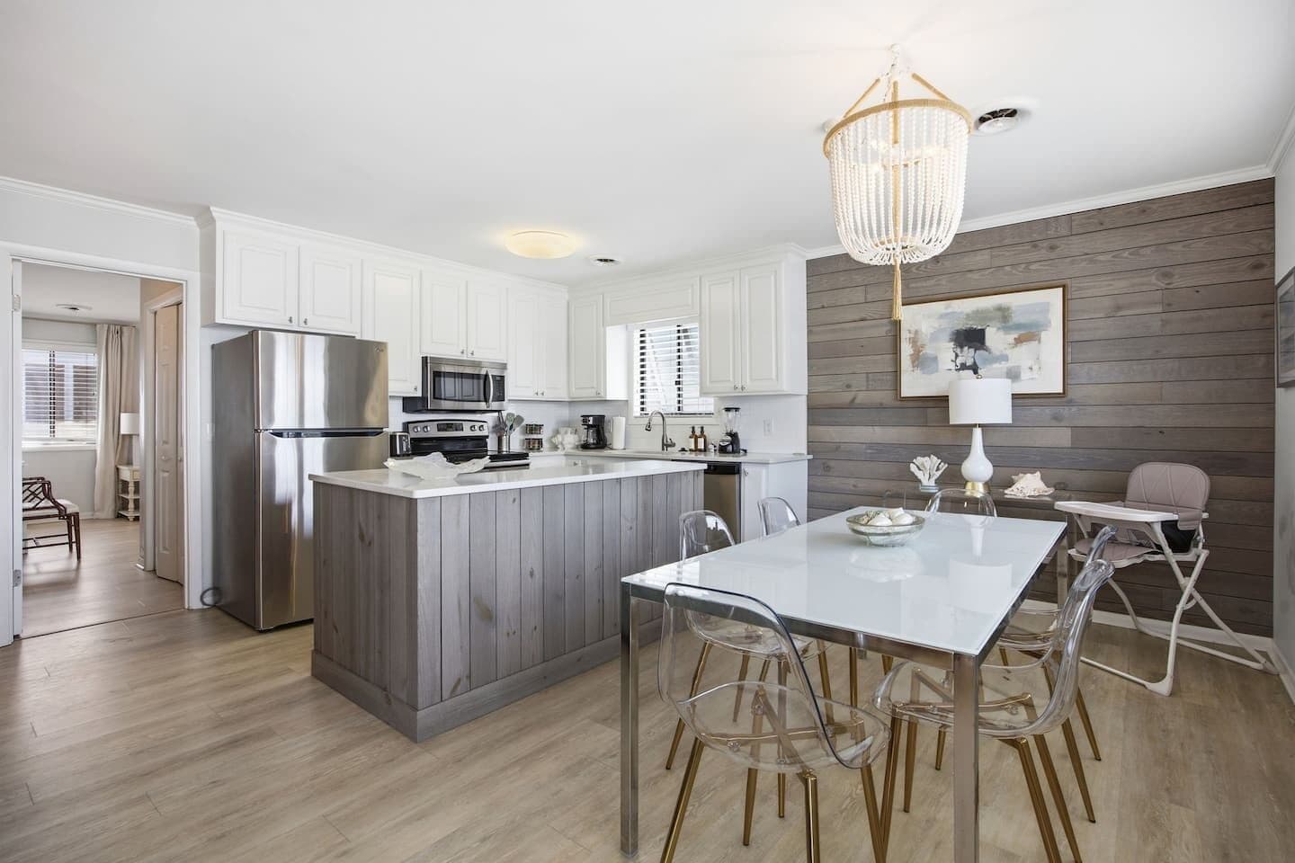 A modern kitchen with white cabinetry, a central island, and a dining area with clear chairs.