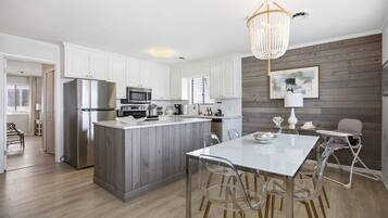A modern kitchen with white cabinetry, a central island, and a dining area with clear chairs.