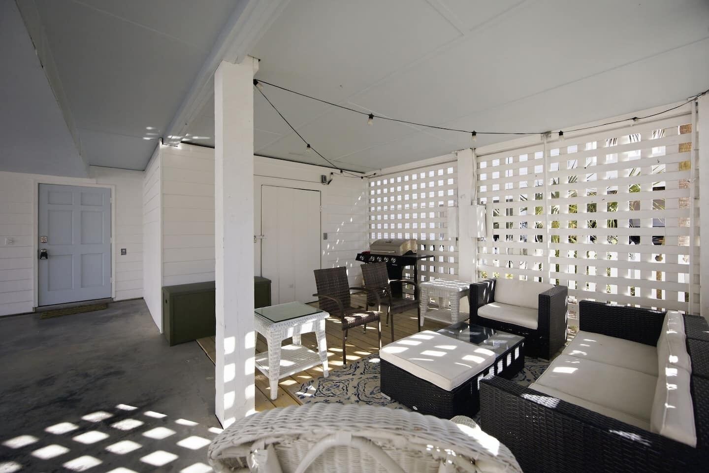 A covered outdoor seating area with wicker furniture, a grill, and a white lattice partition.